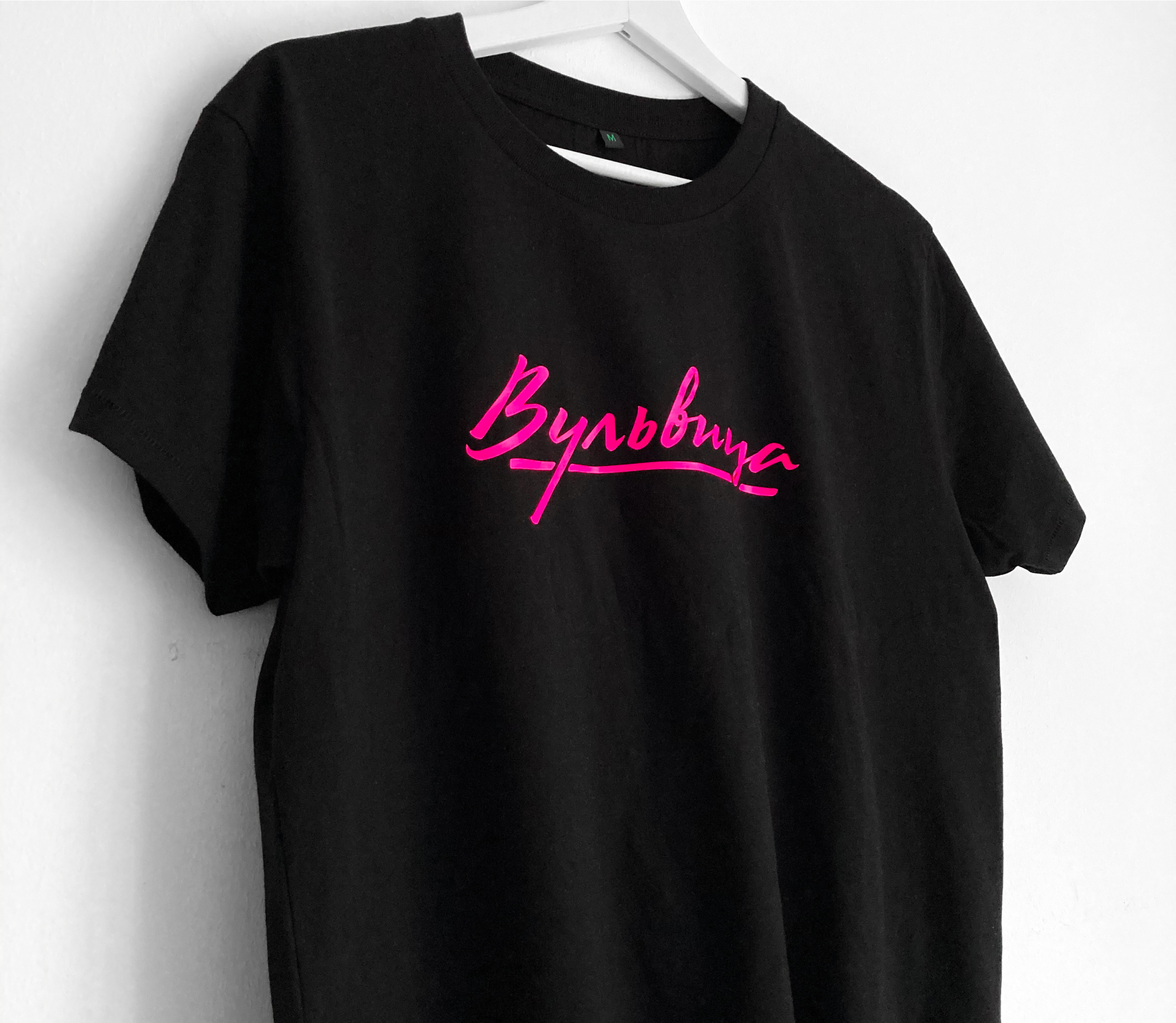 Black t-shirt with a hot pink Cyrillic Vulvitsa script logo on a hanger