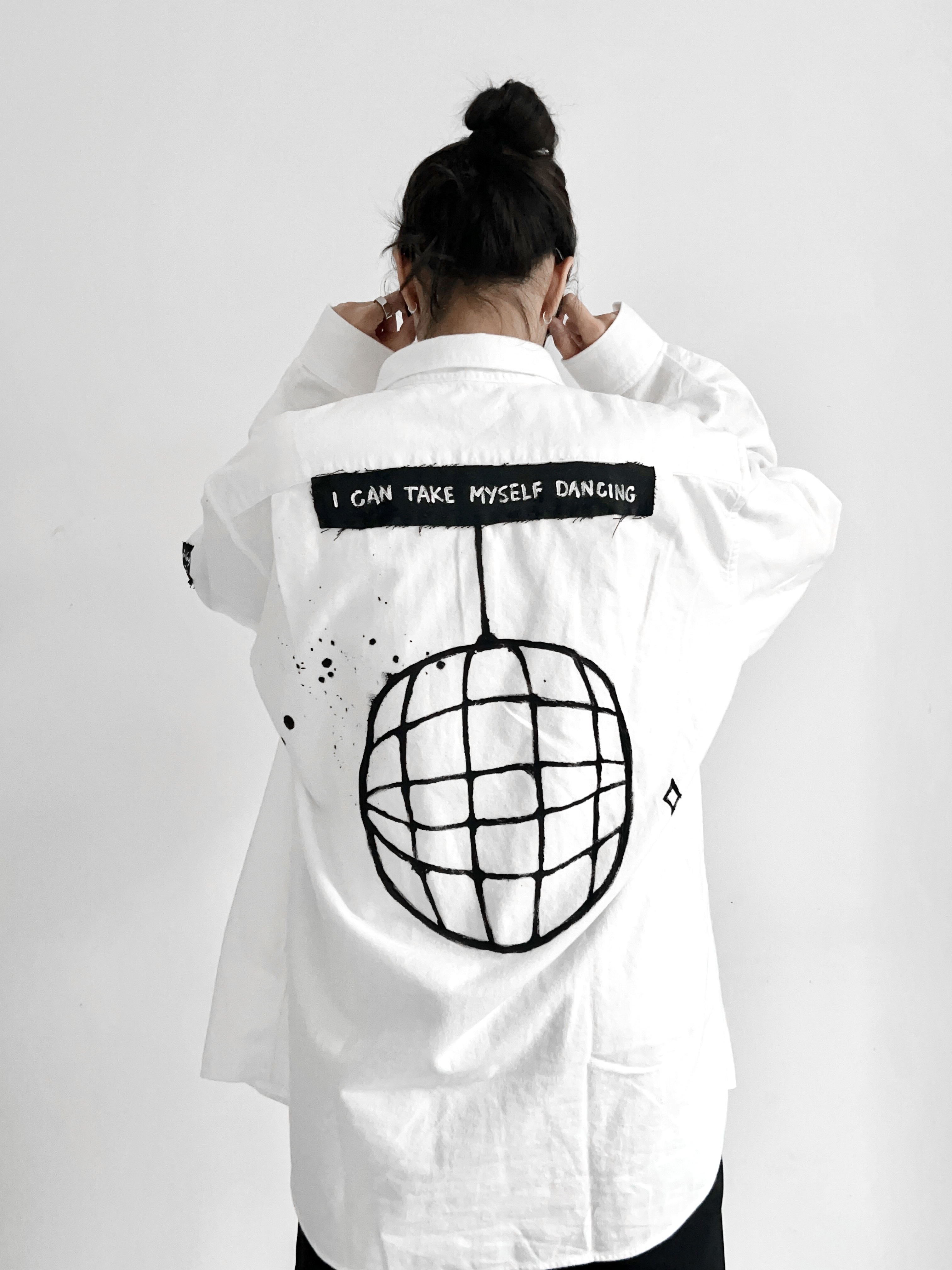 White shirt with an I CAN TAKE MYSELF DANCING patch and a hand-drawn disco ball illustration on the back
