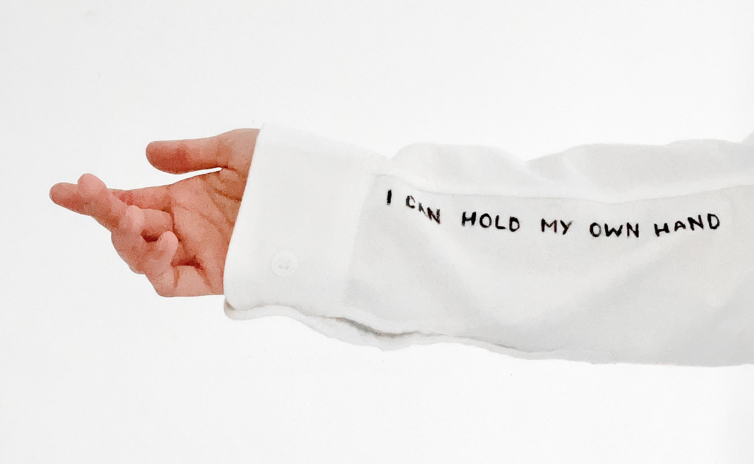 White shirt sleeve with I CAN HOLD MY OWN HAND hand-lettered text and an open palm extended